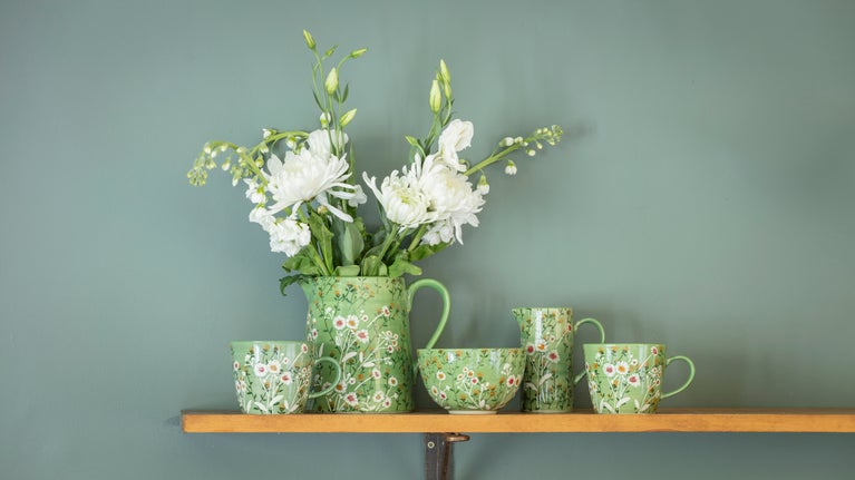 A selection of green ceramic mugs, jugs and a bowl all decorated with a white daisy pattern from the 2025 autumn/winter collection
